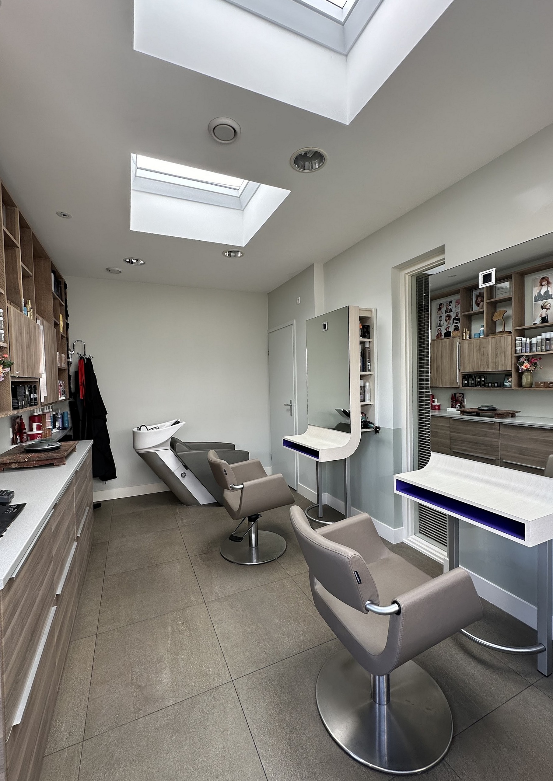 De salon onder de lichtkoepels, met twee kappersstoelen, wasunit en witte werkbladen